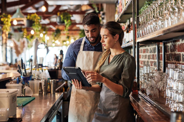 man and woman consulting a tablet behind the counter at a restaurant